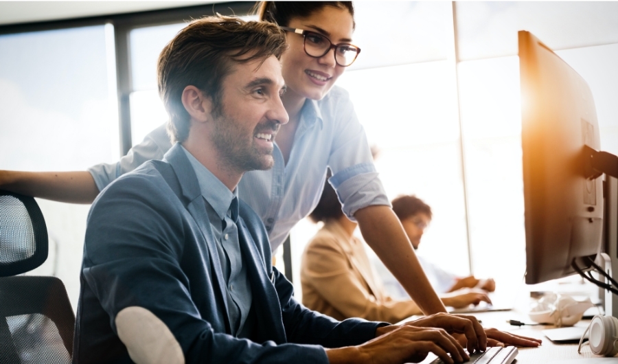 man and woman coworkers looking at computer screen smiling