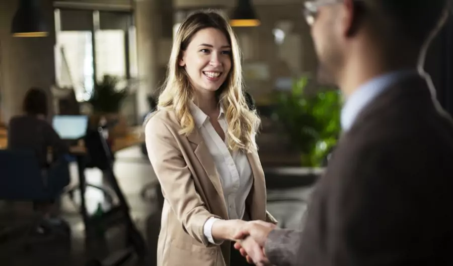 Image of a woman with long blond hair shaking the hand of an out of focus man with a suit